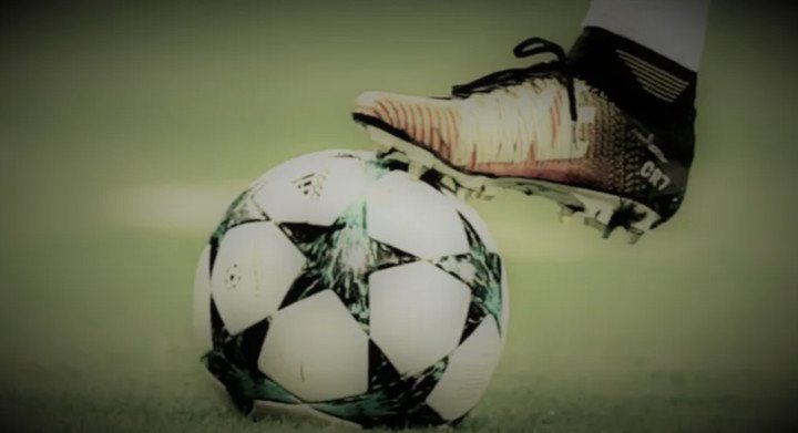 Football bal on the pitch with player's foot on it